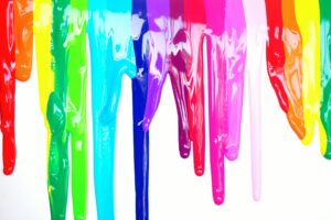Bright, colorful paints dripping creating a rainbow effect on a white background, symbolizing diversity and creativity.