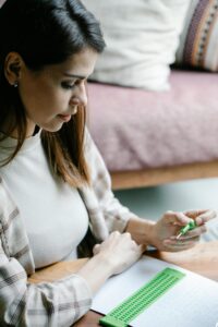 Focused woman using a stylus and slate to write braille at a cozy indoor setting.
